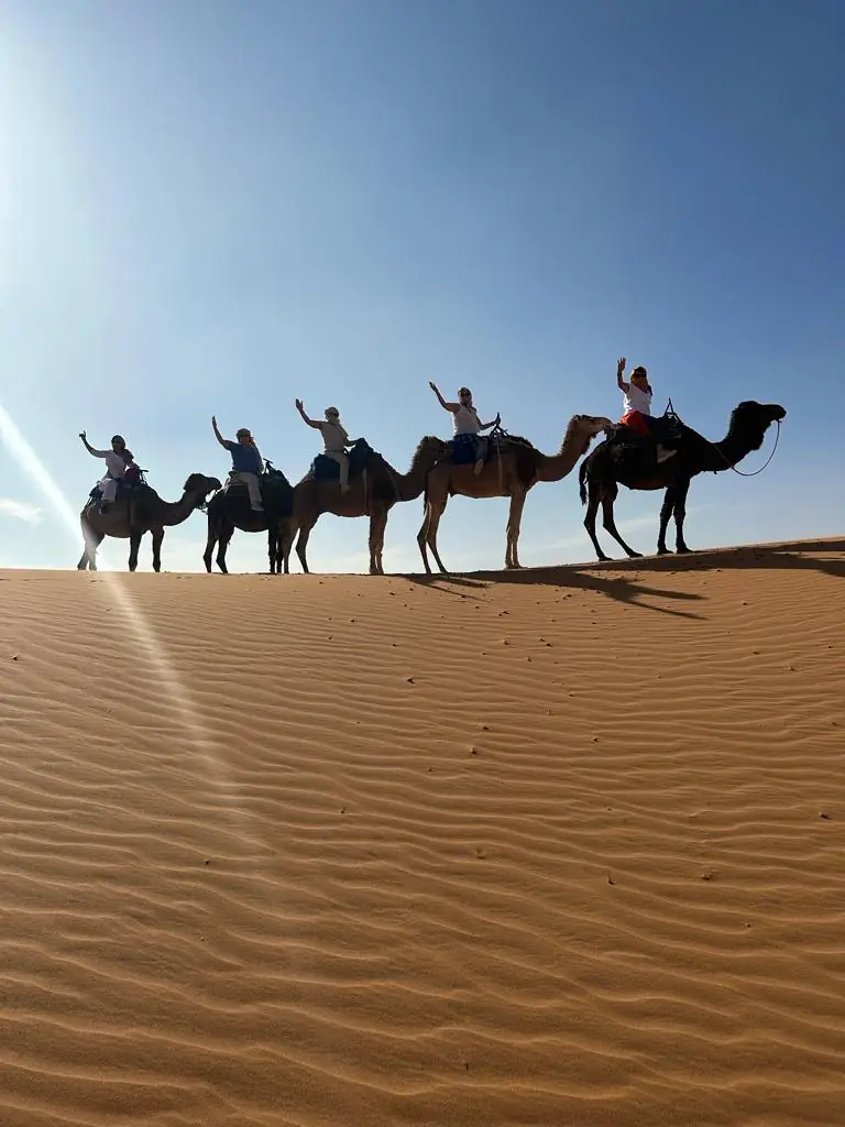 Viajeras saludando desde camellos en las dunas del desierto